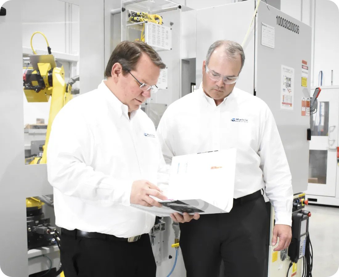 Two men in white Matrix Design logowear in front of a robotic automation cell