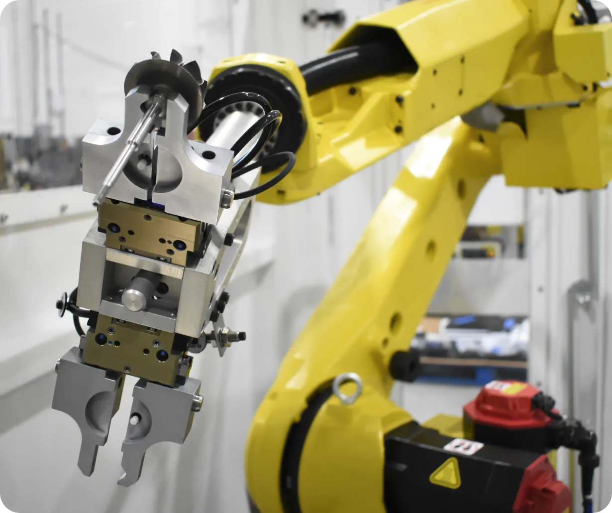Yellow industrial robotic arm with a metallic gripper tooling, operating in a factory setting for part handling and assembly